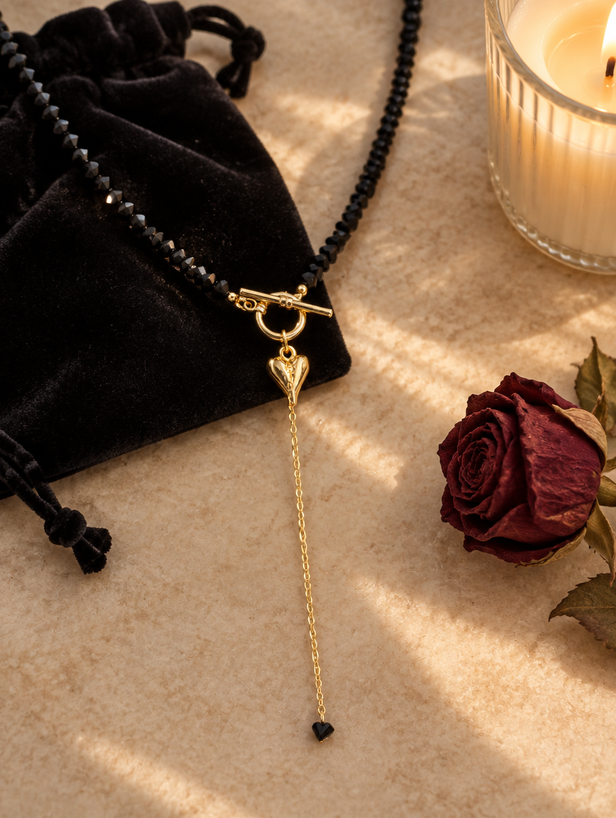 Black bead lariat necklace on a velvet pouch beside a dried rose and candle