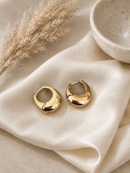Chunky gold-tone oval hoop earrings in a styled still life with props