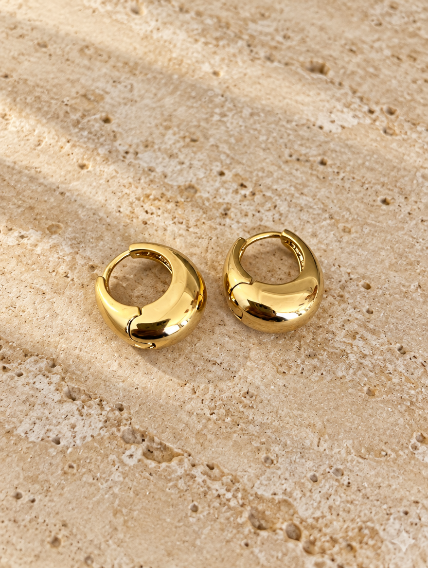 Chunky gold-tone oval hoop earrings lying flat on a soft styled surface