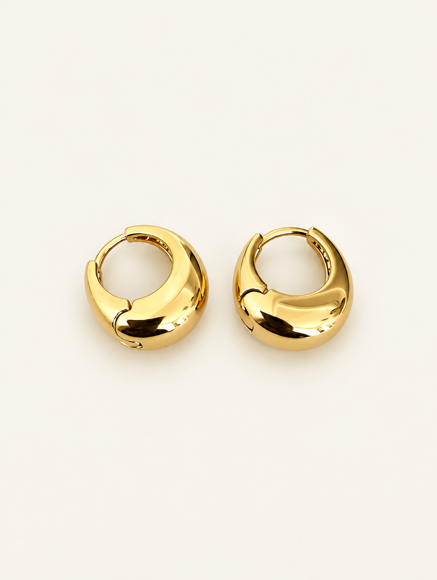 Pair of chunky gold-tone oval hoop earrings on a warm off-white background