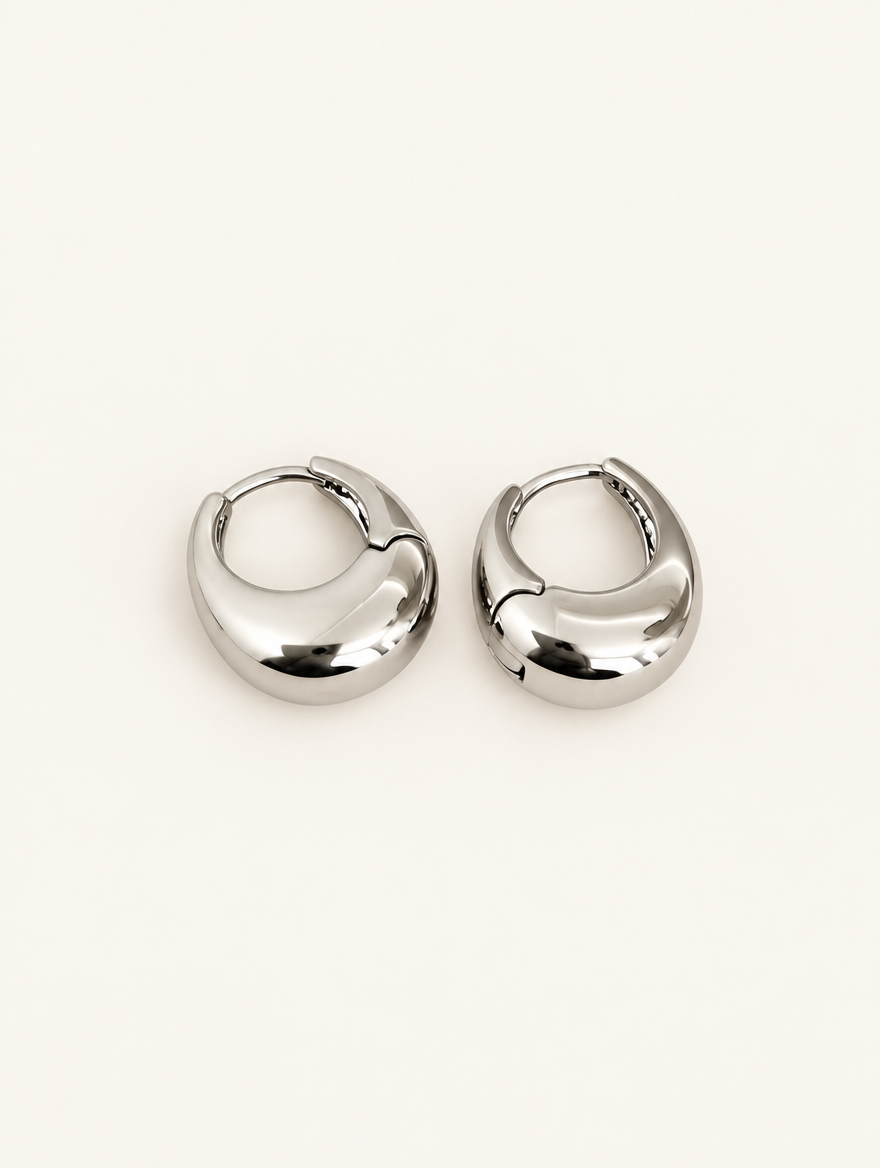 Pair of chunky silver-tone oval hoop earrings on a warm off-white background