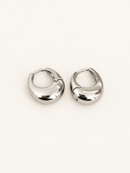 Pair of chunky silver-tone oval hoop earrings on a warm off-white background