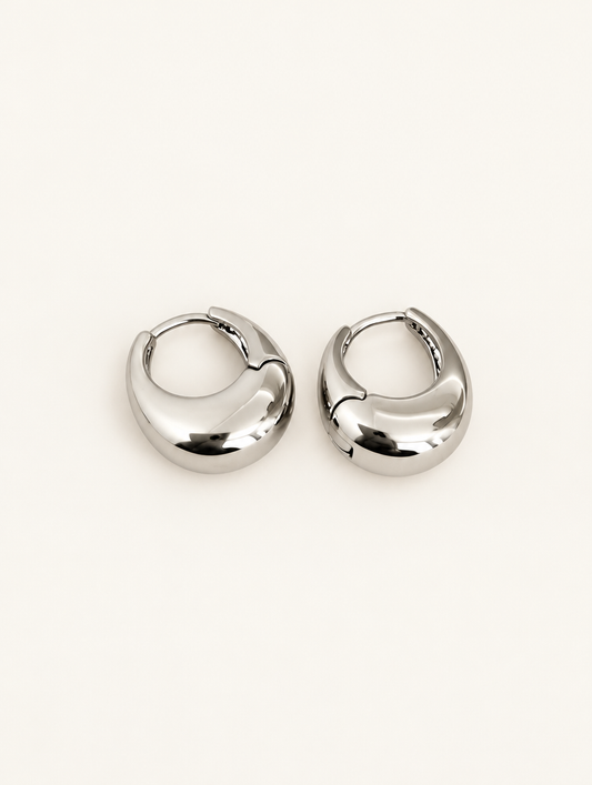 Pair of chunky silver-tone oval hoop earrings on a warm off-white background