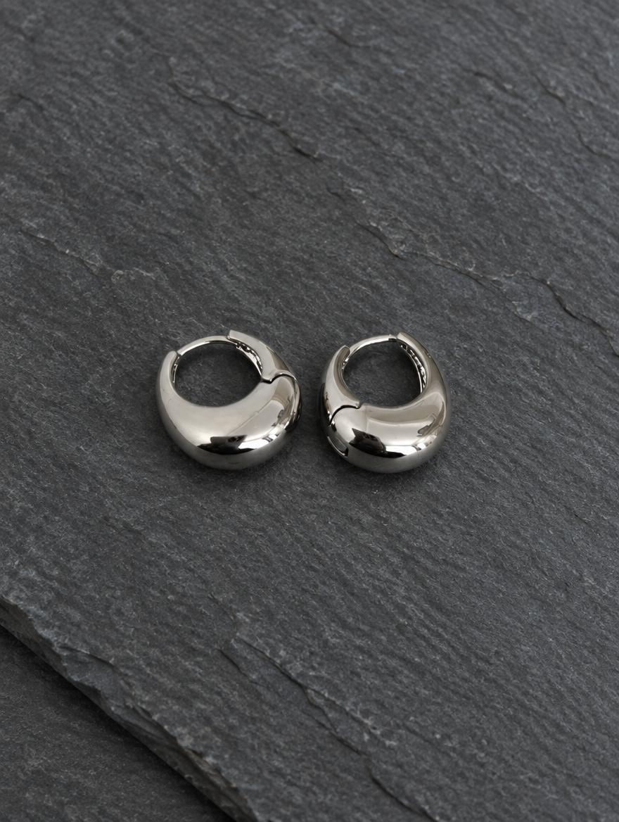 Chunky silver-tone oval hoop earrings lying flat on a soft styled surface