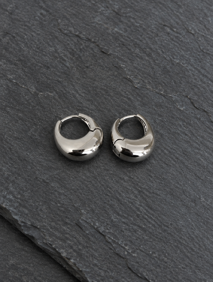 Chunky silver-tone oval hoop earrings lying flat on a soft styled surface