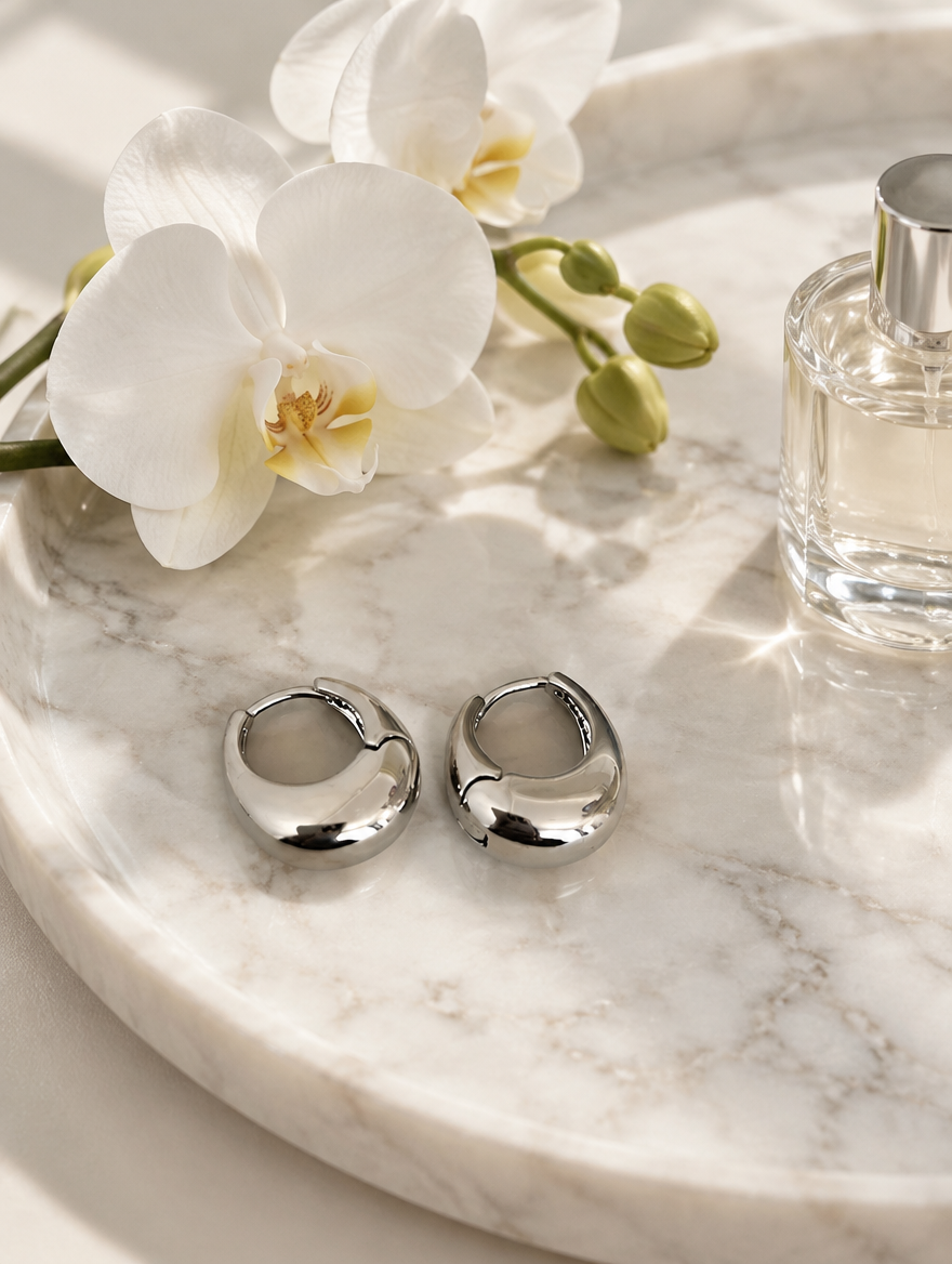 Chunky silver-tone oval hoop earrings in a styled still life with props