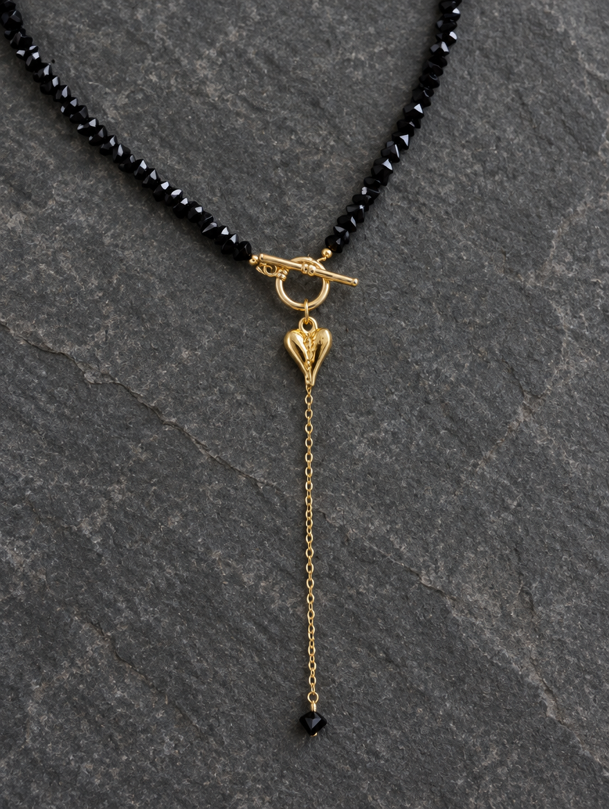 Black bead lariat necklace lying on dark grey stone