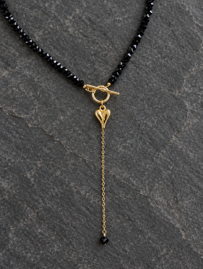 Black bead lariat necklace lying on dark grey stone