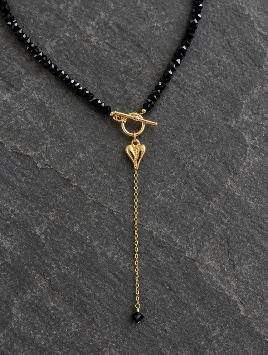 Black bead lariat necklace lying on dark grey stone