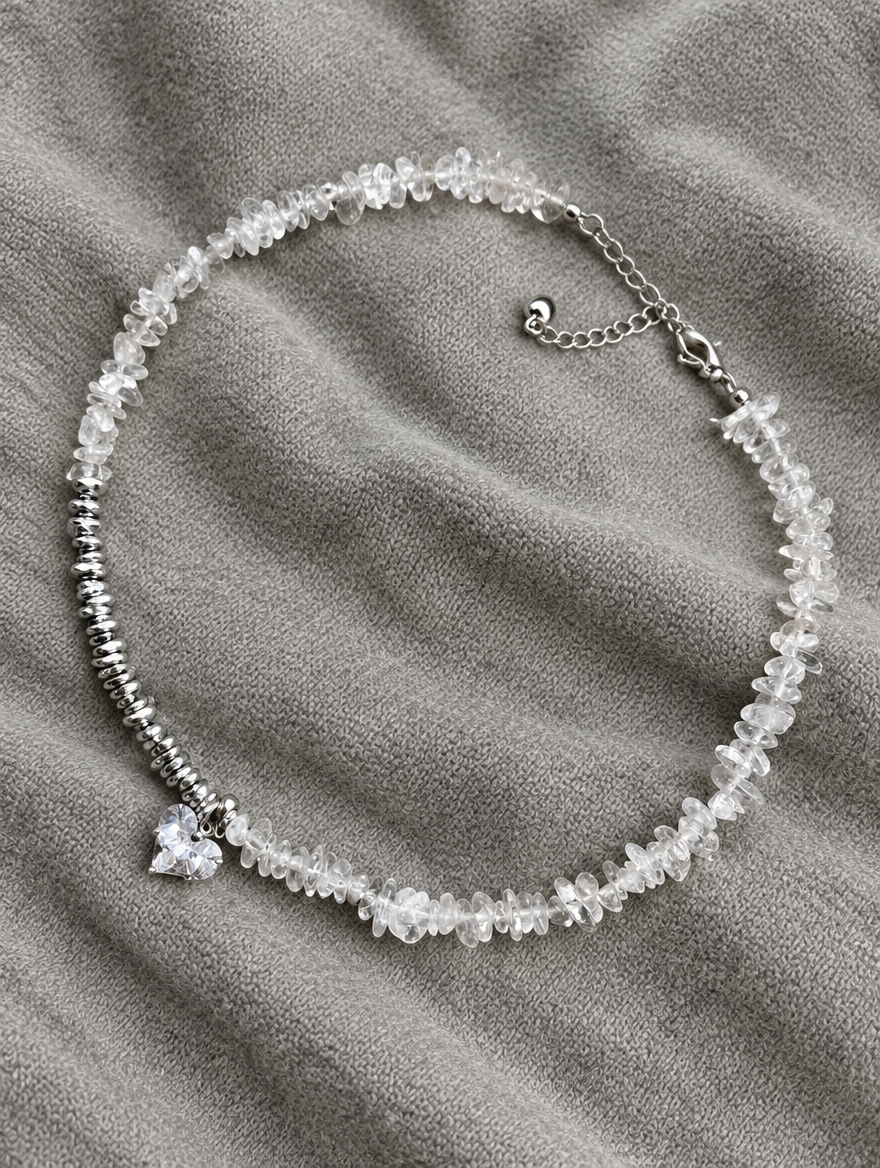 Clear bead choker necklace with heart charm lying on soft grey knit