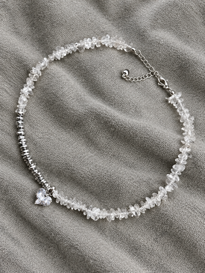 Clear bead choker necklace with heart charm lying on soft grey knit