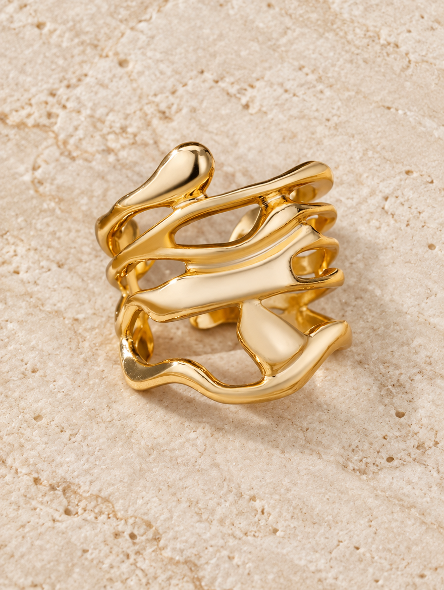 Wide gold wavy open ring resting on a soft textured surface