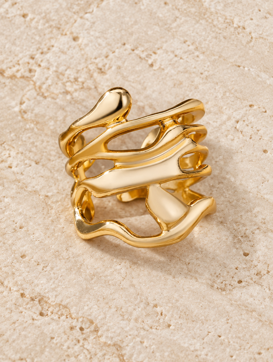Wide gold wavy open ring resting on a soft textured surface