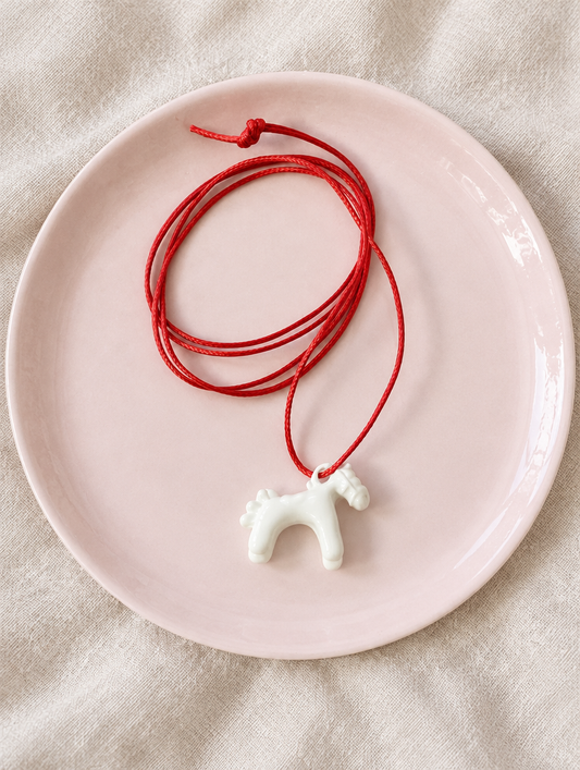 White horse pendant cord necklace on a pale pink plate