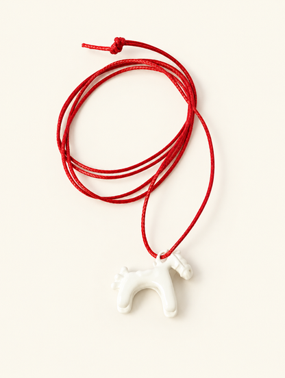 White horse pendant on a red cord necklace on a neutral background