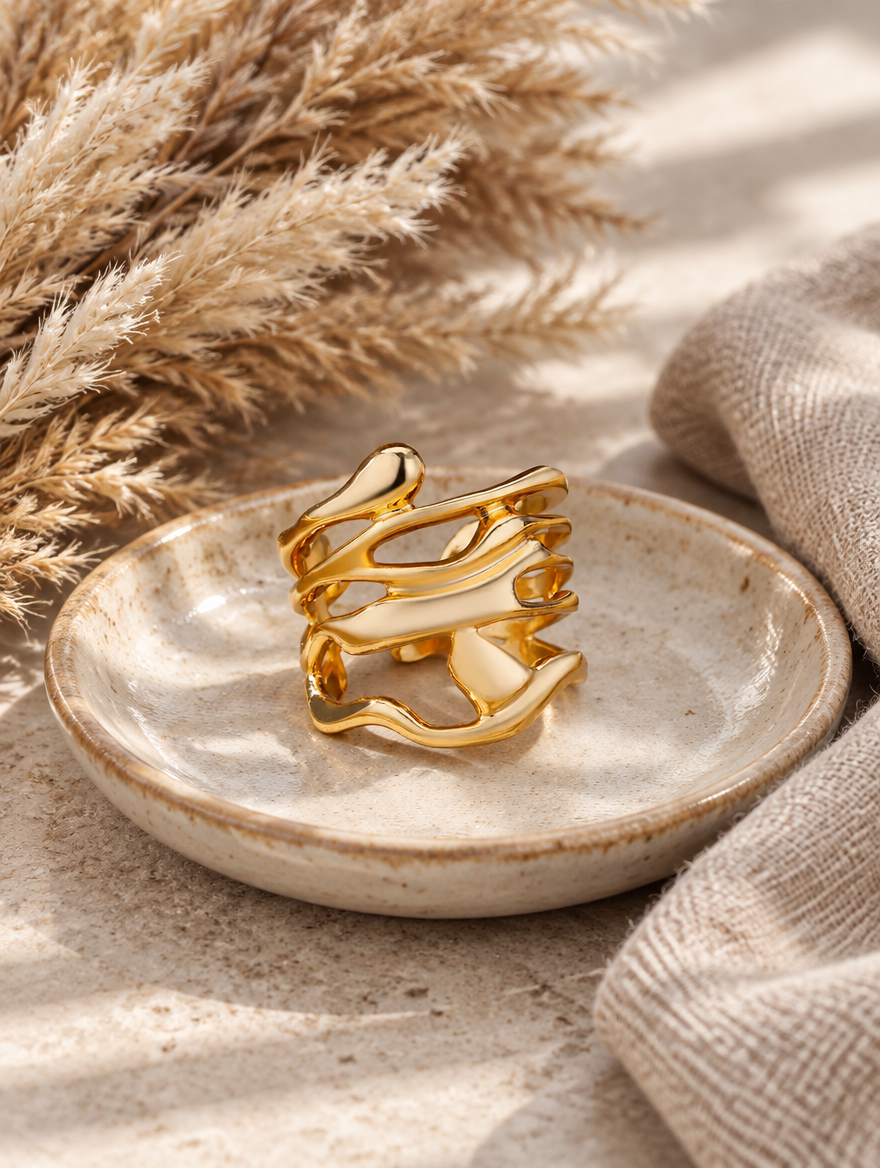 Wide gold wavy open ring in a small dish with styling props