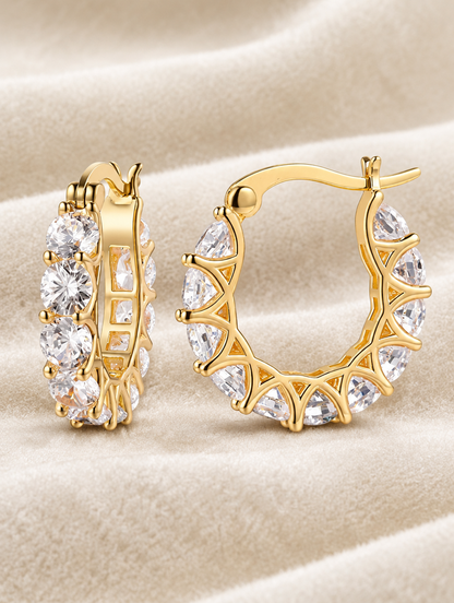 Gold zirconia hoop earrings lying flat on a soft styled surface