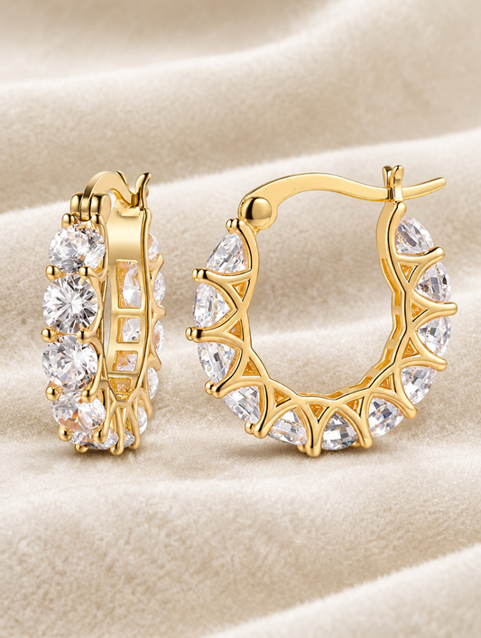 Gold zirconia hoop earrings lying flat on a soft styled surface