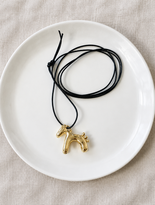 Gold horse pendant cord necklace on a white ceramic plate