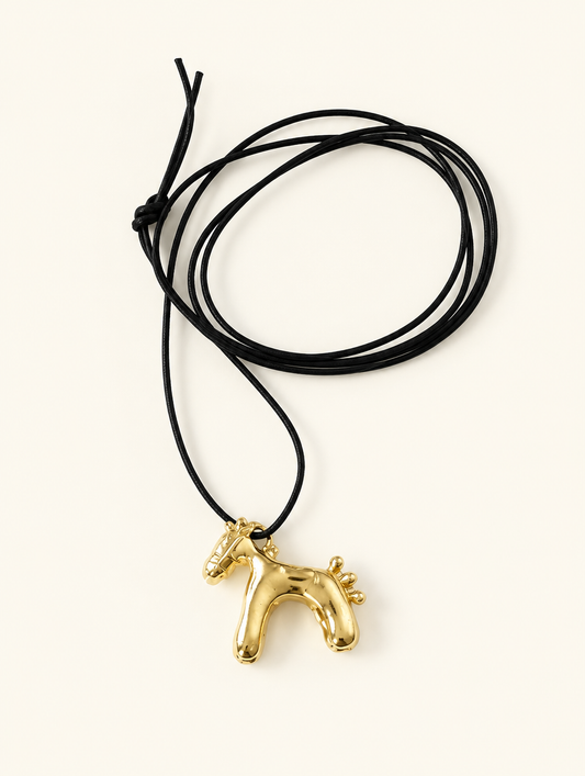 Gold-tone horse pendant on a black cord necklace on a neutral background