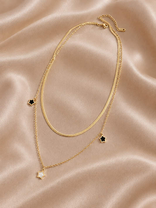 Gold layered necklace with star charms lying on champagne silk