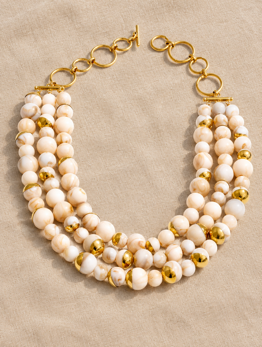 Cream beaded collar necklace lying on sand-coloured linen