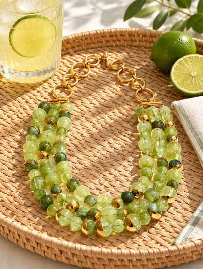 Green beaded statement necklace on a woven tray with lemonade and limes
