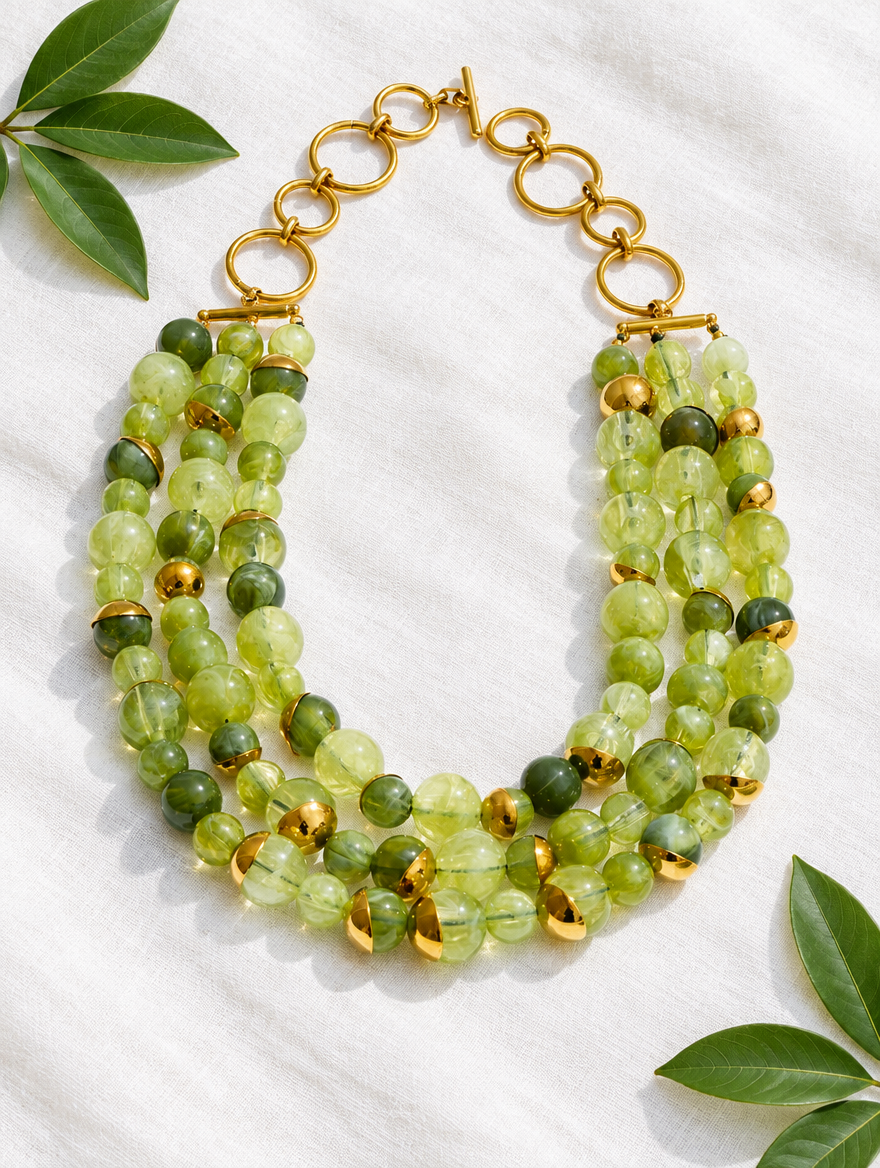 Green beaded collar necklace lying on white linen with leaves