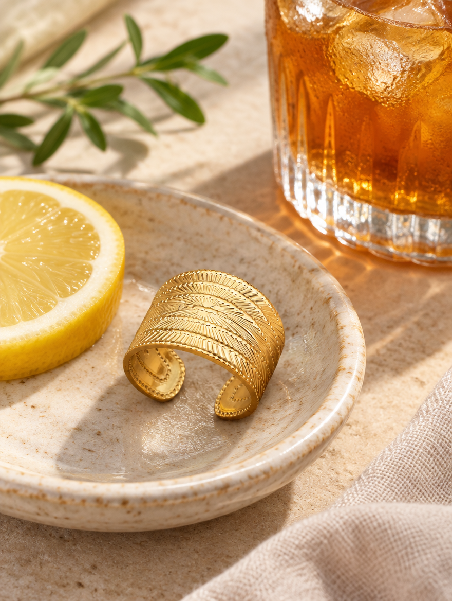 Wide gold ribbed open ring in a small dish with styling props