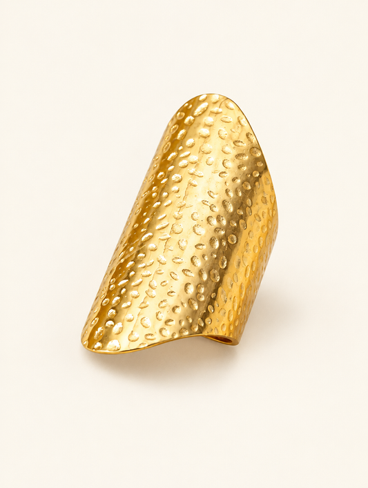 Wide gold hammered shield ring on a neutral background