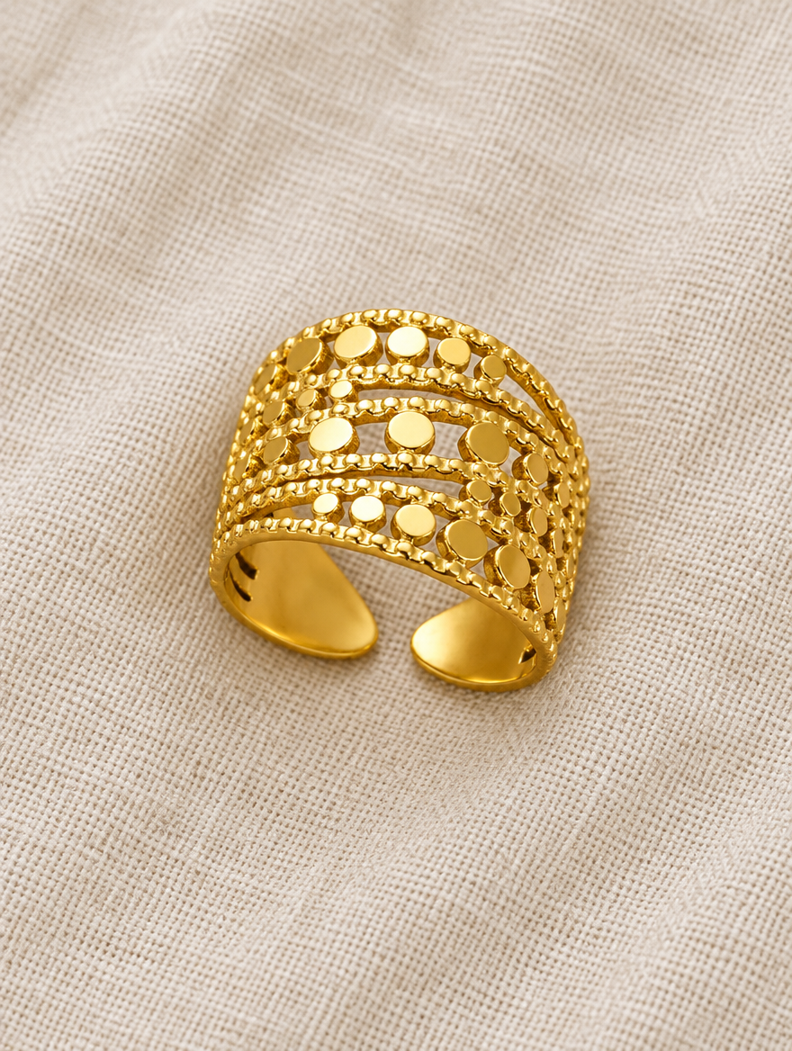 Wide gold disc texture open ring resting on a soft textured surface