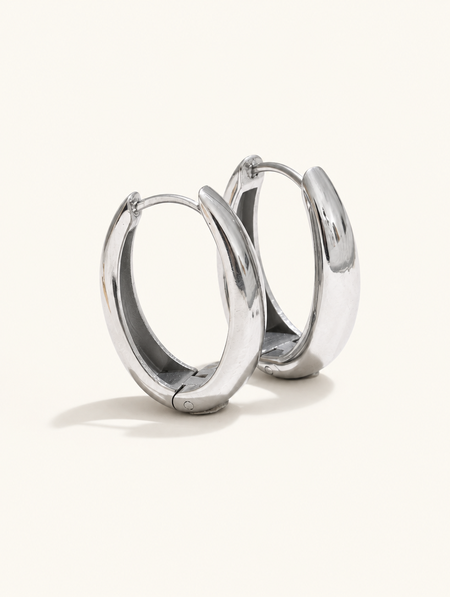 Pair of 316l steel silver huggie hoop earrings on a warm off-white background