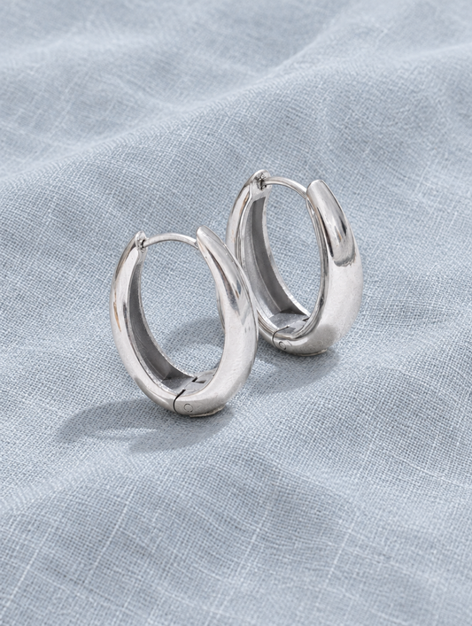 316l steel silver huggie hoop earrings lying flat on a soft styled surface