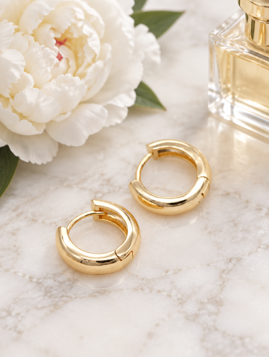 Gold-plated chunky huggie hoop earrings in a styled still life with props