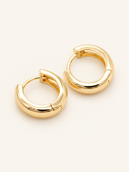 Pair of gold-plated chunky huggie hoop earrings on a warm off-white background