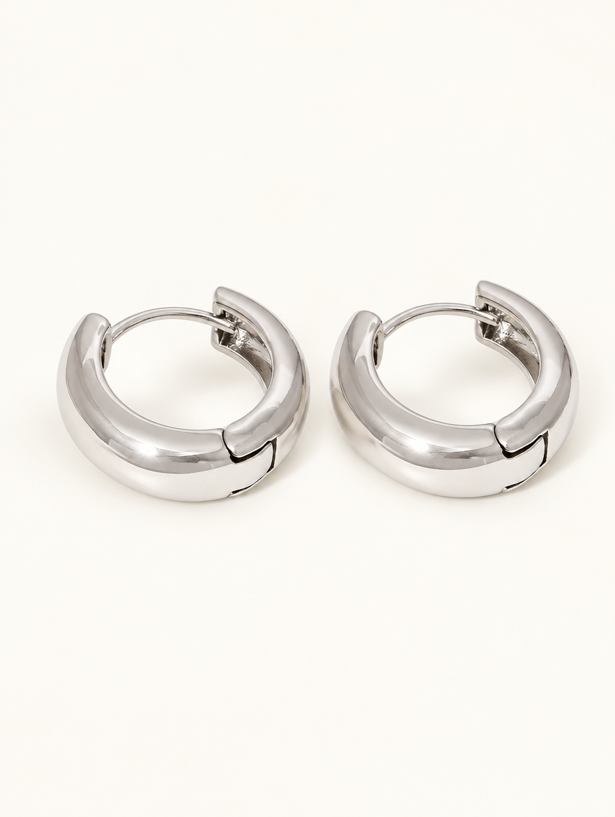 Pair of silver-tone chunky huggie hoop earrings on a warm off-white background