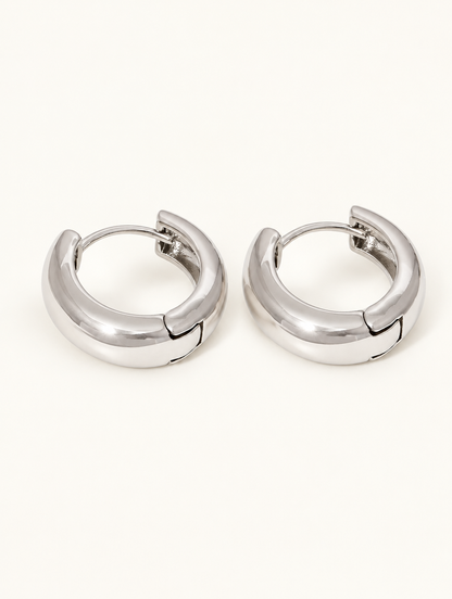 Pair of silver-tone chunky huggie hoop earrings on a warm off-white background