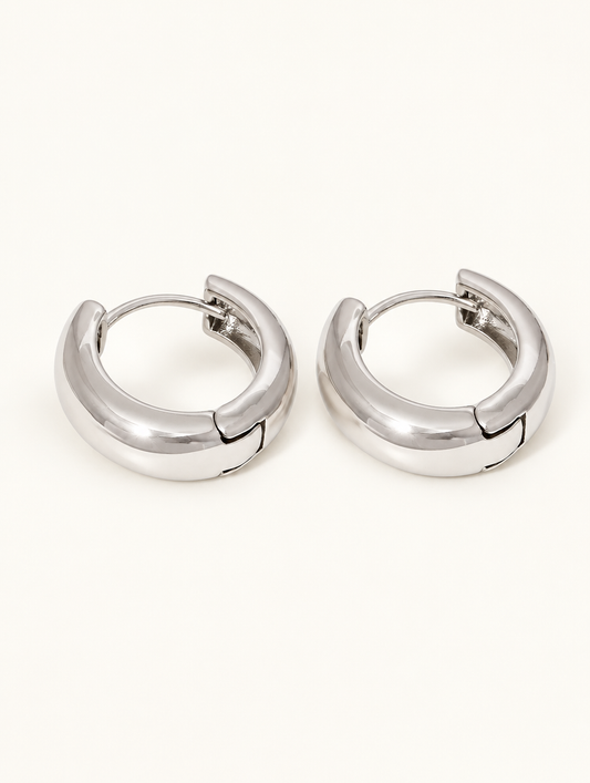 Pair of silver-tone chunky huggie hoop earrings on a warm off-white background