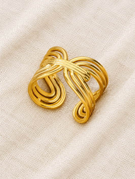 Gold twisted ribbon open ring resting on a soft textured surface