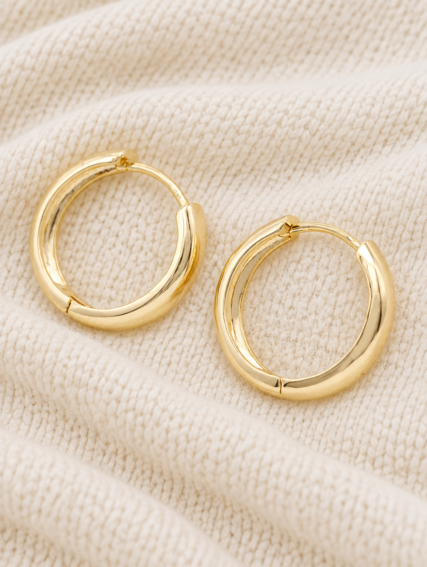 Gold-plated large smooth hoop earrings lying flat on a soft styled surface