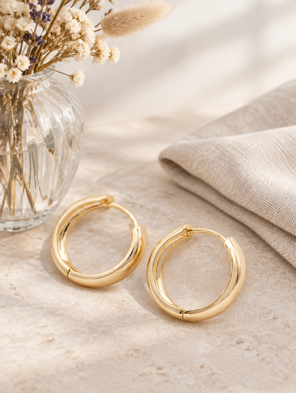 Gold-plated large smooth hoop earrings in a styled still life with props
