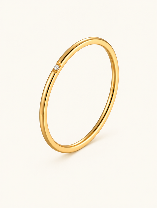 Thin gold stacking ring with a single zirconia on a neutral background