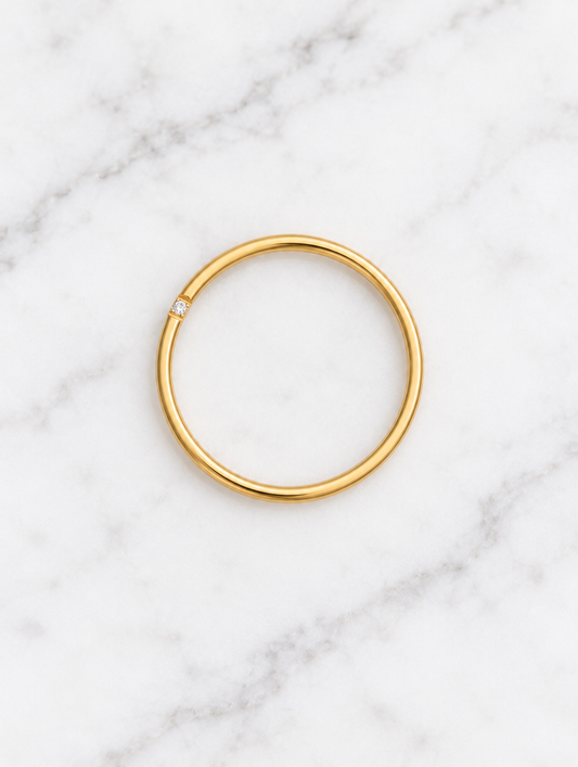Thin gold stacking ring with a single zirconia resting on a soft textured surface