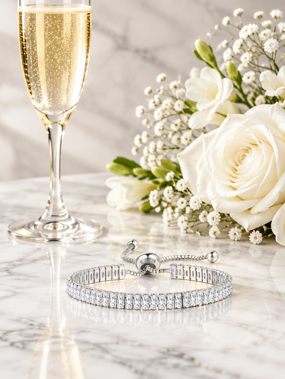 Silver slider bracelet beside a champagne flute and white flowers on marble