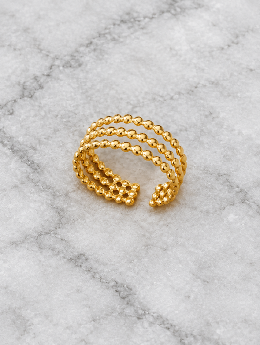 Gold triple row beaded open ring resting on a soft textured surface