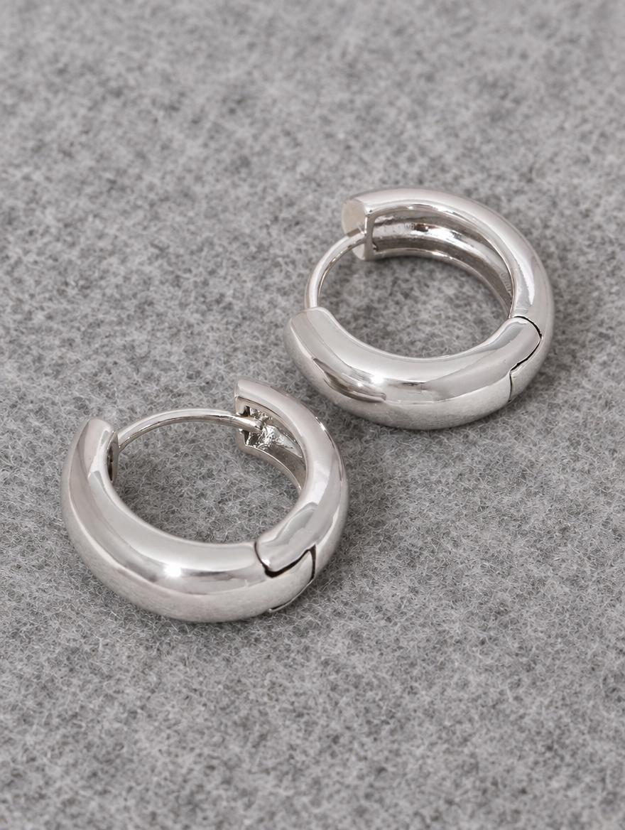 Silver-tone chunky huggie hoop earrings lying flat on a soft styled surface