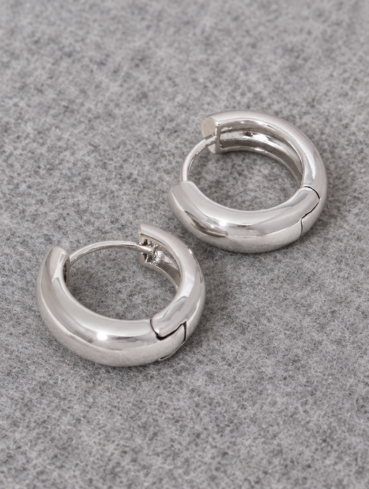 Silver-tone chunky huggie hoop earrings lying flat on a soft styled surface