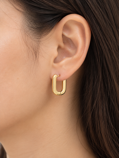 Woman wearing a gold-plated rounded rectangle huggie earring