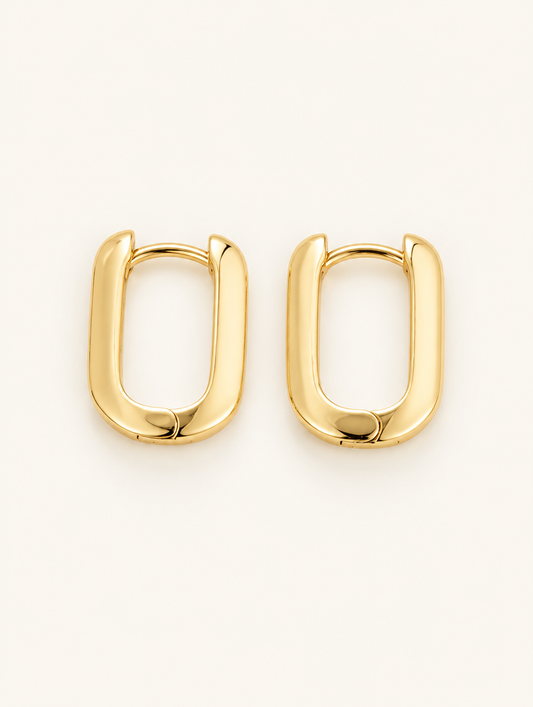 Pair of gold-plated rounded rectangle huggie earrings on a warm off-white background
