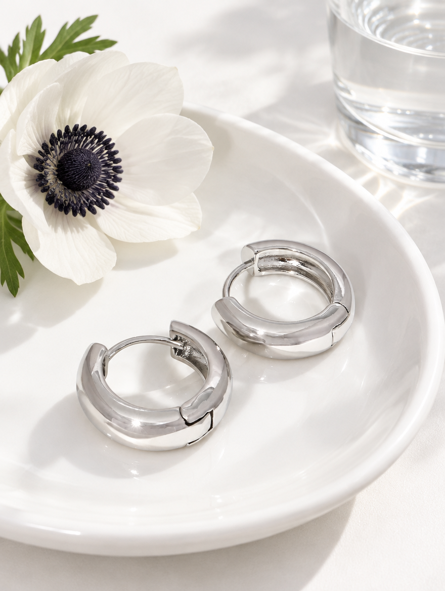 Silver-tone chunky huggie hoop earrings in a styled still life with props